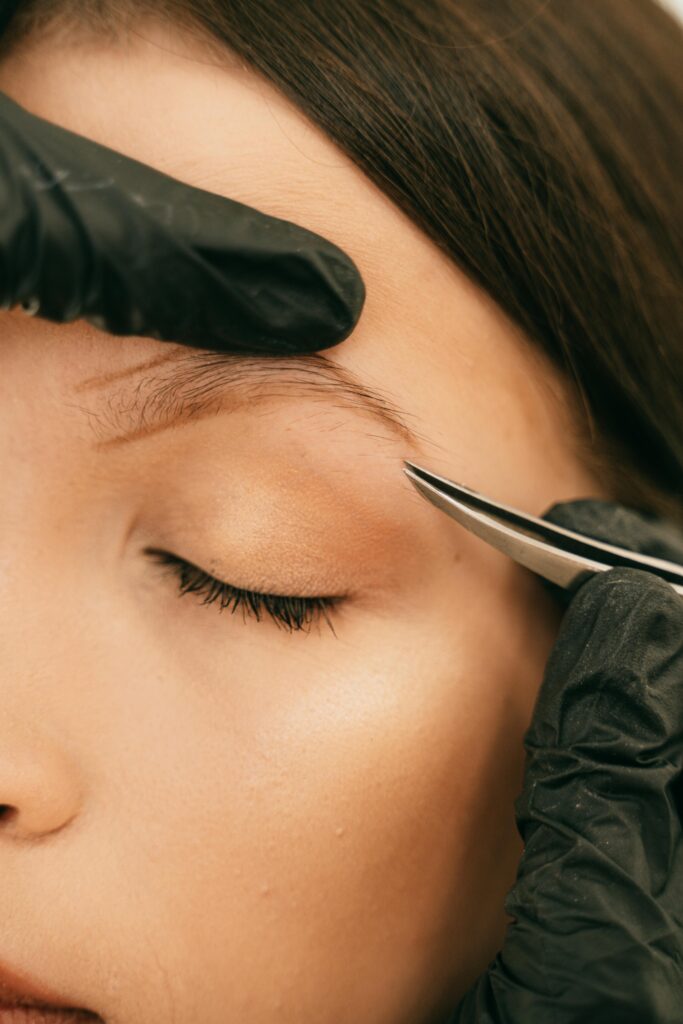 A detailed close-up of a woman having her eyebrow shaped with tweezers, highlighting professional beauty care.